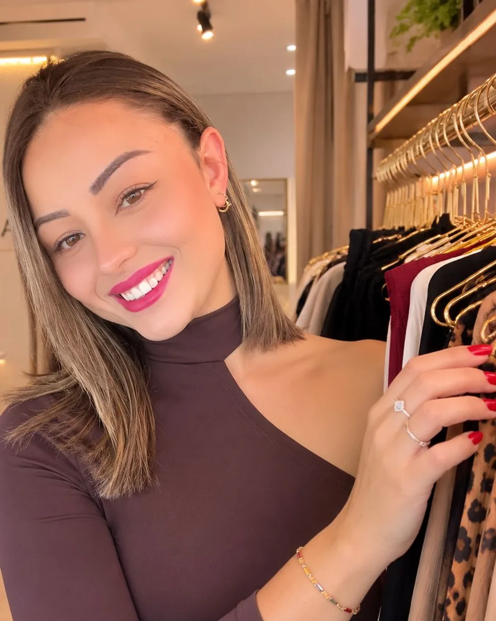 Bruna, da Vicenza Modas, sorrindo ao lado de uma arara de peças na loja em São Marcos